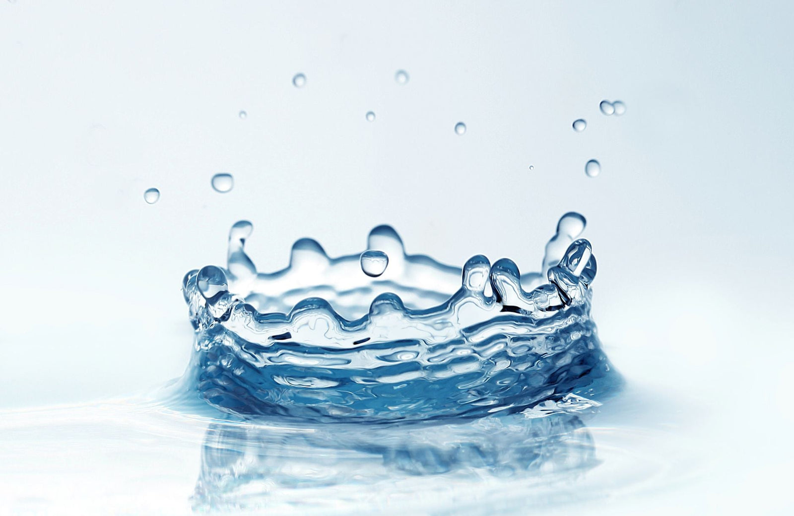 A crown-shaped splash of clear water frozen mid-motion against a soft pale blue background