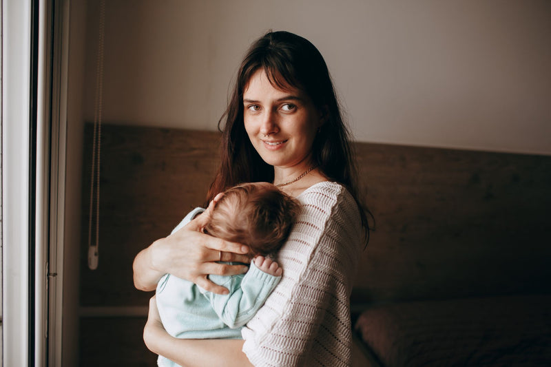 A mother holding her sleeping newborn by a bright window.