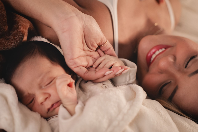 A mother and her newborn holding hands in a tender close moment.