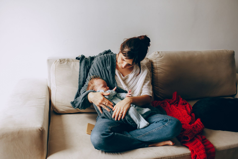 A mother holding her sleeping newborn close on a cozy sofa at home.