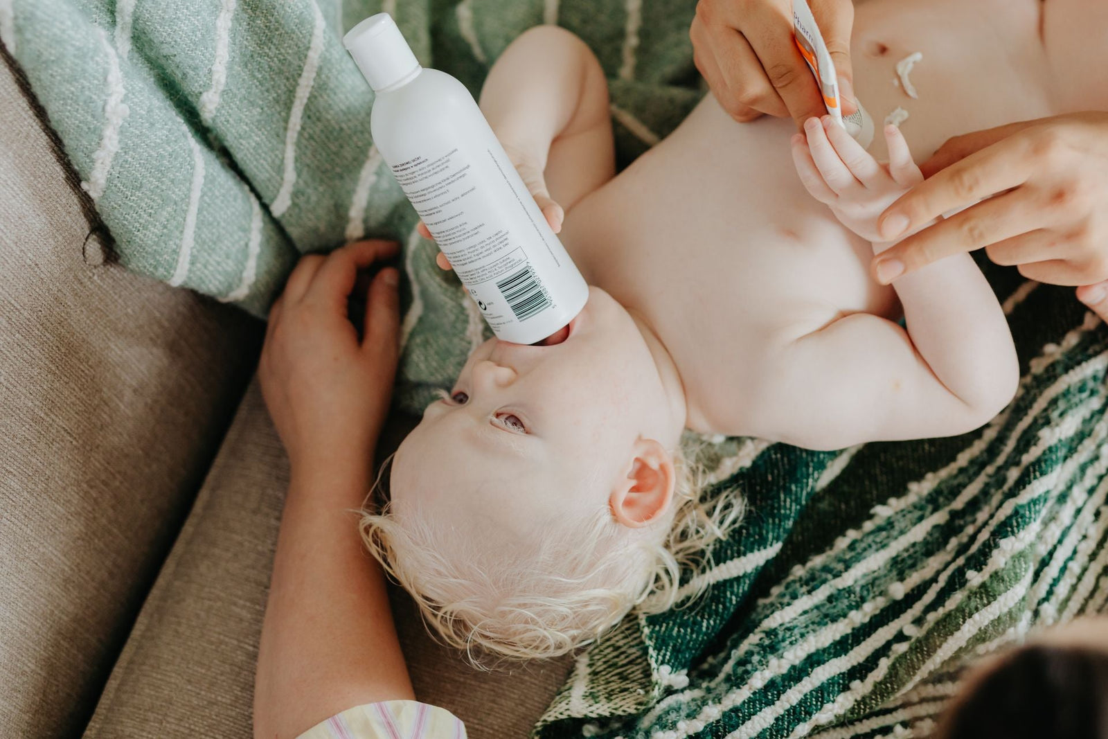 A baby lying comfortably holding a lotion bottle during gentle skin care.