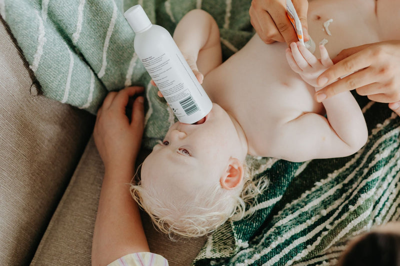 A baby lying comfortably holding a lotion bottle during gentle skin care.
