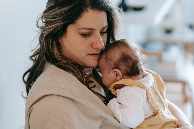 A mother gently holding her newborn close, soft light in a calm room.