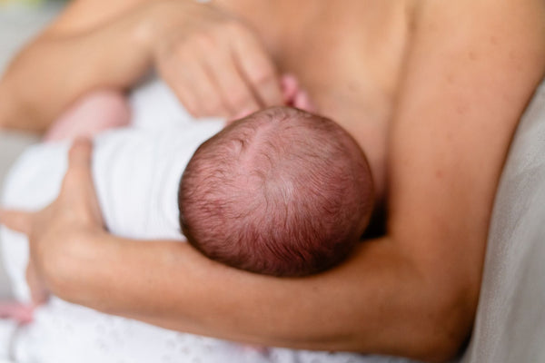 A mother breastfeeding her newborn in soft, bright light.