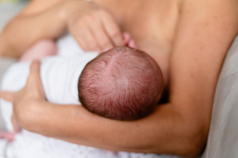 A mother breastfeeding her newborn in soft, bright light.