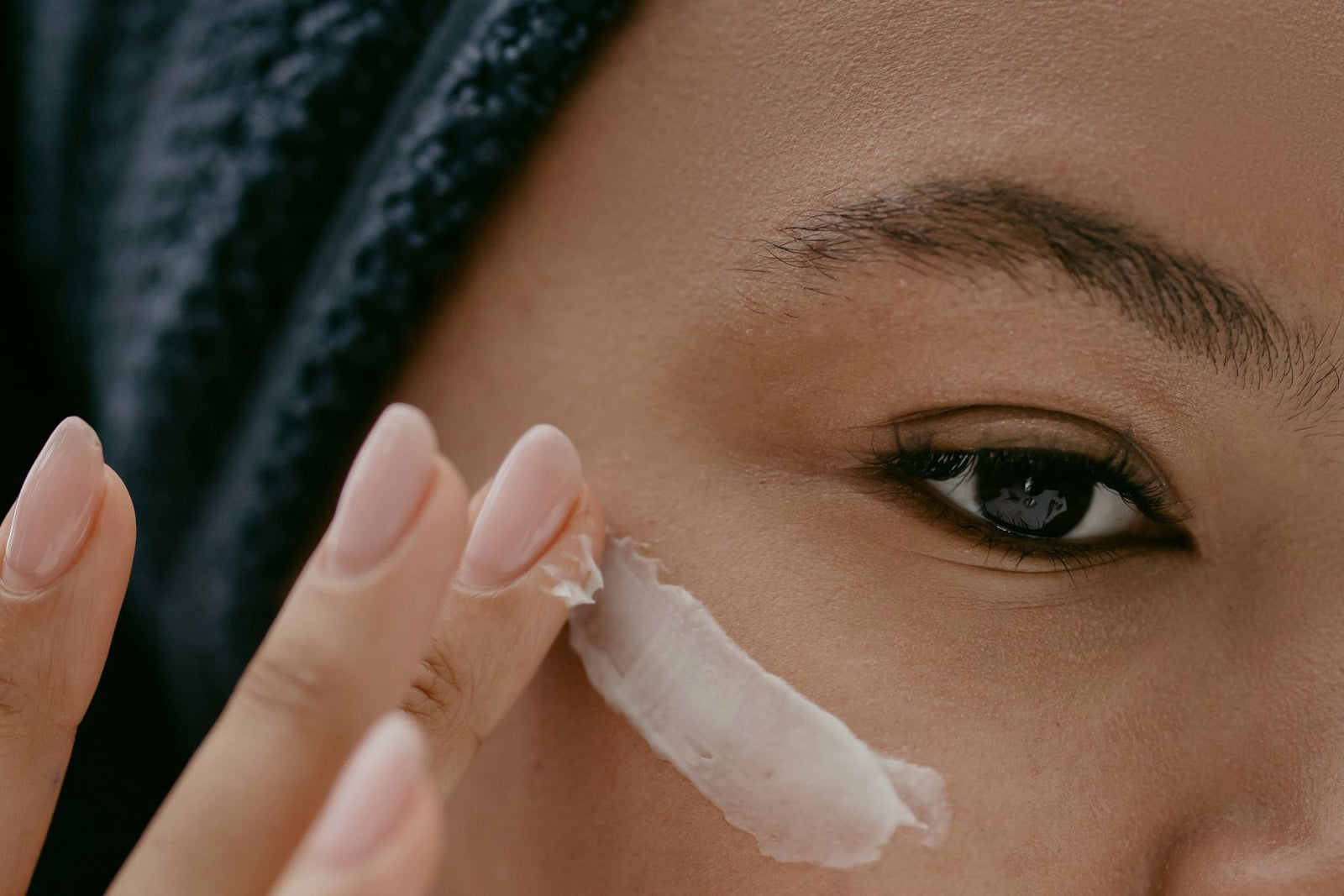Extreme close-up of a woman applying a cooling gel with her fingertip along the under-eye area.